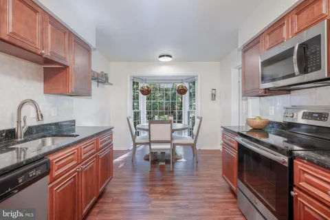 a kitchen with stainless steel appliances granite countertop a stove top oven a sink dishwasher a dining table and chairs with wooden floor