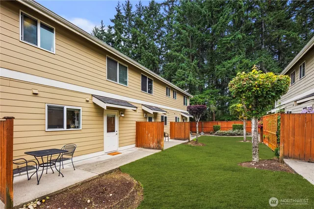 a backyard of a house with table and chairs floor to ceiling window and wooden fence