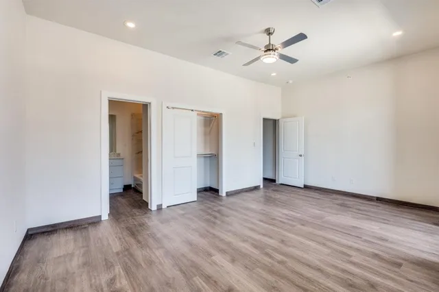 a view of an empty room with wooden floor and a ceiling fan