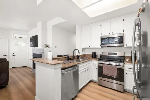 a kitchen with stainless steel appliances granite countertop a stove top oven a sink and white cabinets