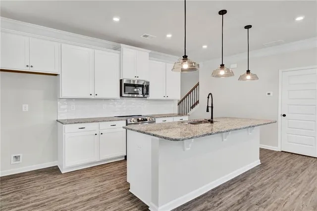 a view of an empty room and kitchen with wooden floor