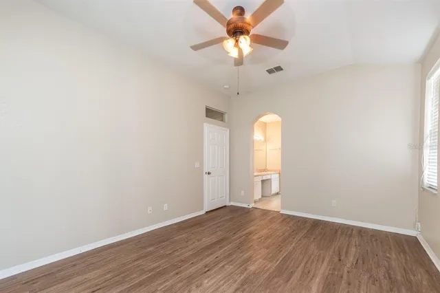 an empty room with wooden floor fan and windows
