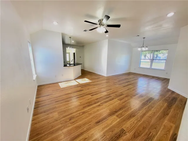 an empty room with wooden floor ceiling fan and windows