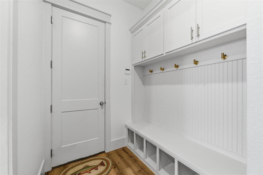 6625 Sandy Beach Road Azle, TX 76020 - Photo 14 of 40 Mudroom features built-in bench seating, cubby storage, wall-mounted hooks, upper cabinetry, and wood-look flooring throughout the space. Functional storage layout provides organization and everyday utility near the interior entry area.