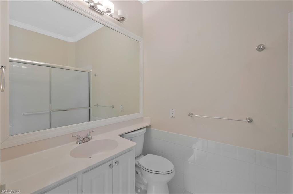 6044 Andros Way Naples, FL 34119 - Photo 19 of 46 Full bath with crown molding, toilet, vanity, a shower with door, and tile walls