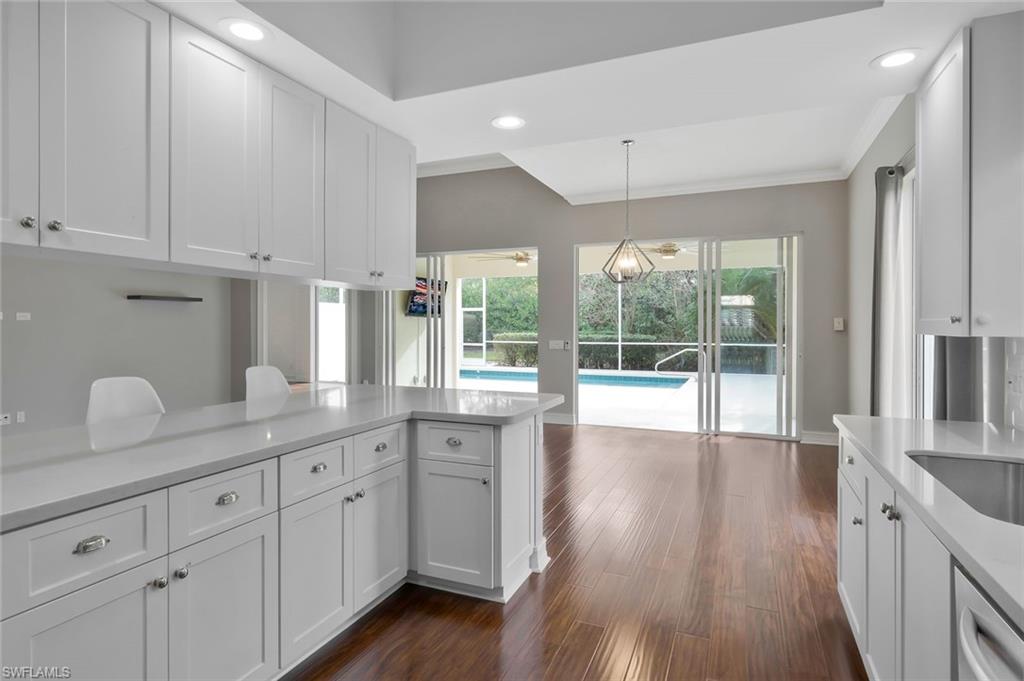 6044 Andros Way Naples, FL 34119 - Photo 5 of 46 Kitchen featuring light countertops, pendant lighting, stainless steel dishwasher, white cabinets, and dark wood-style flooring