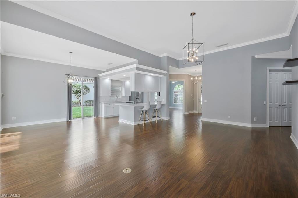 6044 Andros Way Naples, FL 34119 - Photo 10 of 46 Unfurnished living room featuring an inviting chandelier, plenty of natural light, baseboards, and wood finished floors