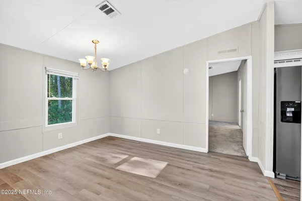 an empty room with wooden floor chandelier and windows