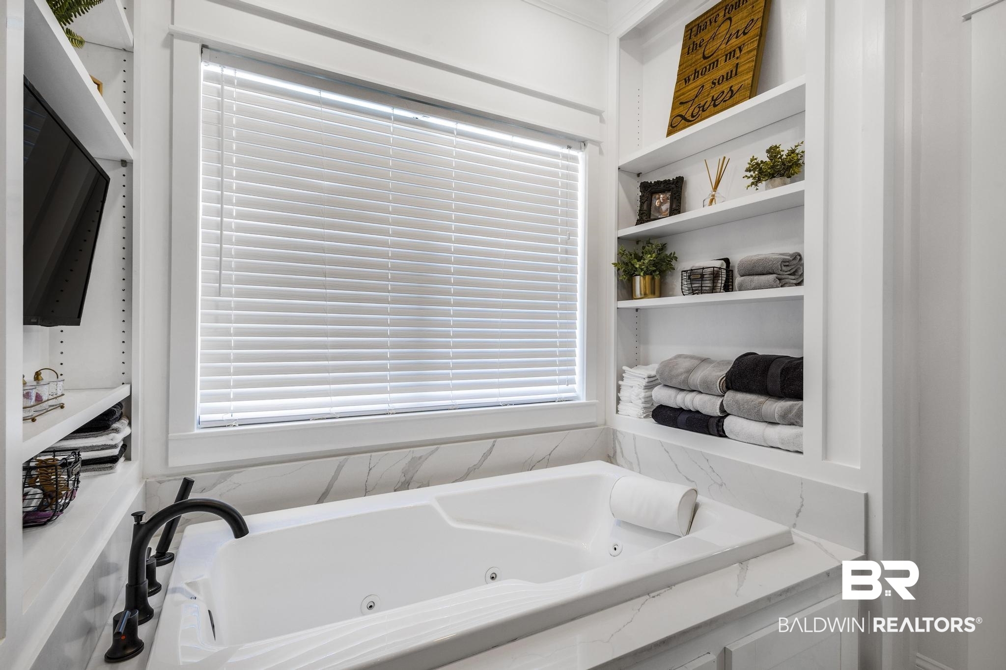83 Caisson Trace Daphne, AL 36527 - Photo 38 of 63 Built-in jetted tub surrounded by a marble-look countertop and backsplash, featuring a black fixture, window with blinds, and integrated shelving