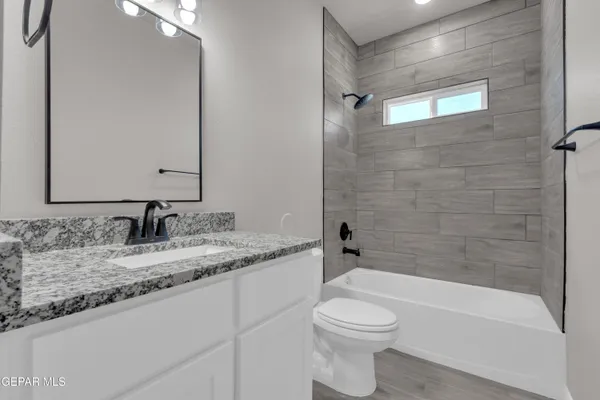 a bathroom with a granite countertop bathtub shower sink vanity and toilet