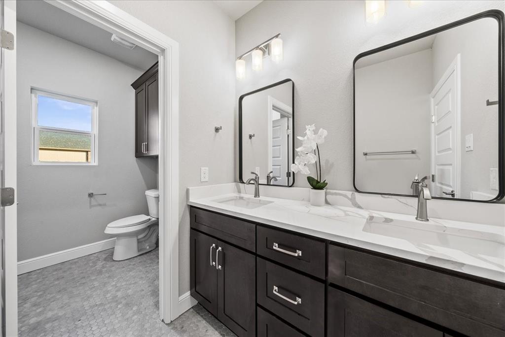 6421 Starlight Ranch Road Godley, TX 76044 - Photo 33 of 39 a bathroom with a granite countertop toilet a double vanity sink and a mirror