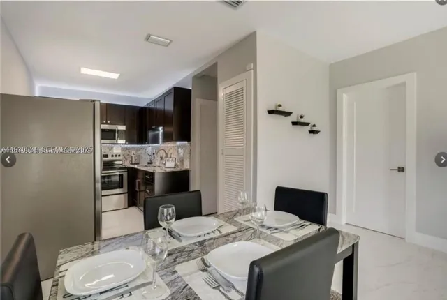 a kitchen with stainless steel appliances kitchen island granite countertop a refrigerator a sink a stove a dining table and chairs