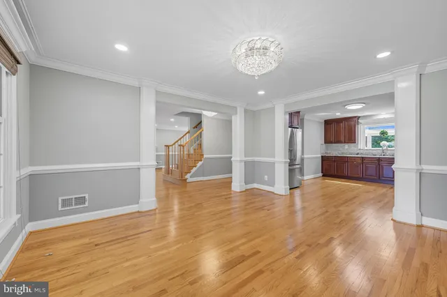 a view of an empty room with wooden floor and a kitchen