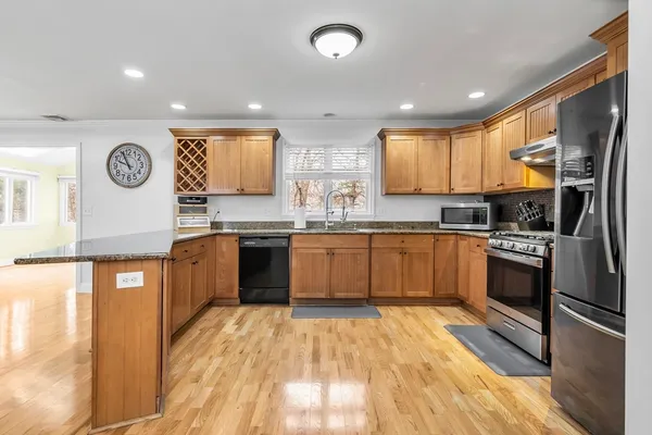 a kitchen with stainless steel appliances granite countertop a stove top oven a sink a dining table and chairs with wooden floor