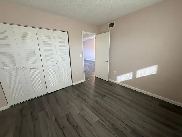 a view of an empty room with wooden floor and closet