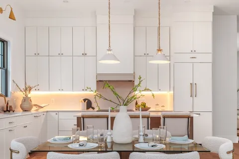 a living room with white couches and kitchen view with wooden floor