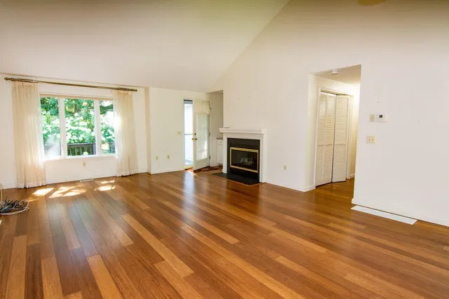 an empty room with wooden floor fireplace and windows