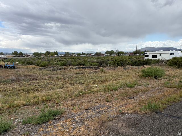 Undisclosed Address Emery, UT 84522 - Photo 2 of 4 Expansive undeveloped land with natural vegetation, featuring distant structures and mountainous terrain under a cloudy sky