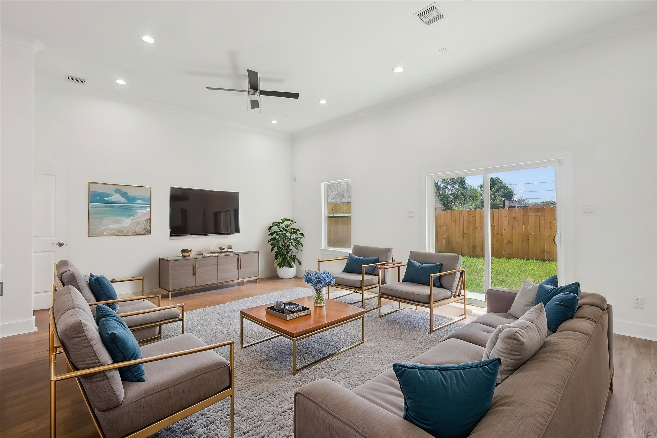 Staged living room with neutral tones, entertainment setup, and sliding glass doors opening to the backyard with natural light.