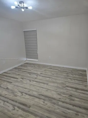 a view of an empty room with wooden floor and a chandelier