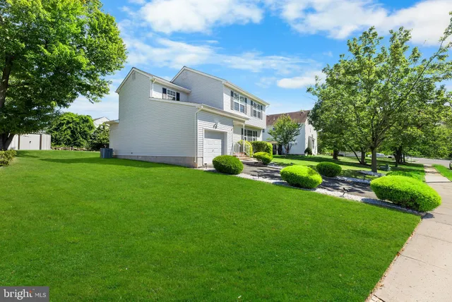 a view of a white house with a big yard plants and large trees