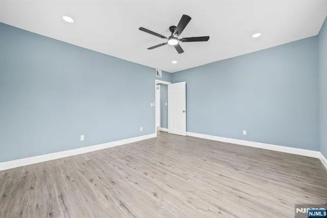 a view of an empty room with wooden floor and a ceiling fan
