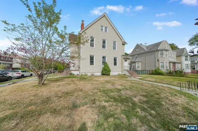 a view of a white house next to a yard with big trees