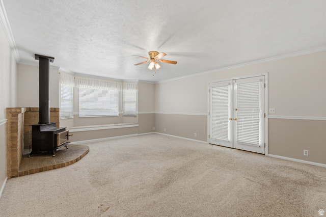 148 Tennyson Avenue Sandy, UT 84070 - Photo 15 of 55 Expansive room featuring a brick-surround wood-burning stove, bay windows with integrated bench seating, neutral carpeting, a ceiling fan, and French doors