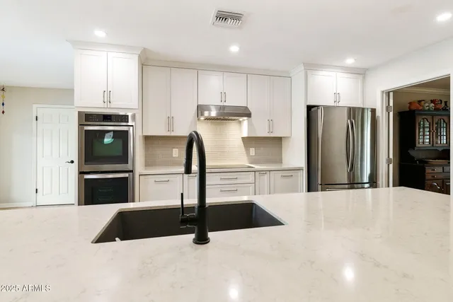a kitchen with stainless steel appliances granite countertop a refrigerator sink and white cabinets