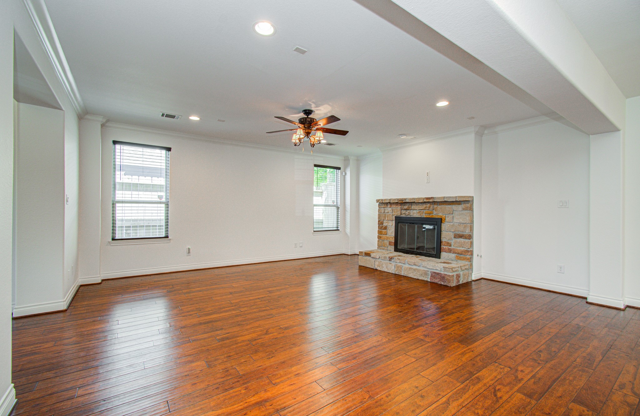 6621 North Main Street Houston, TX 77009 - Photo 9 of 41 This spacious living room features elegant hardwood floors, a cozy stone fireplace, recessed lighting, and a ceiling fan. The room is bright with natural light from large windows, offering a welcoming and open atmosphere.