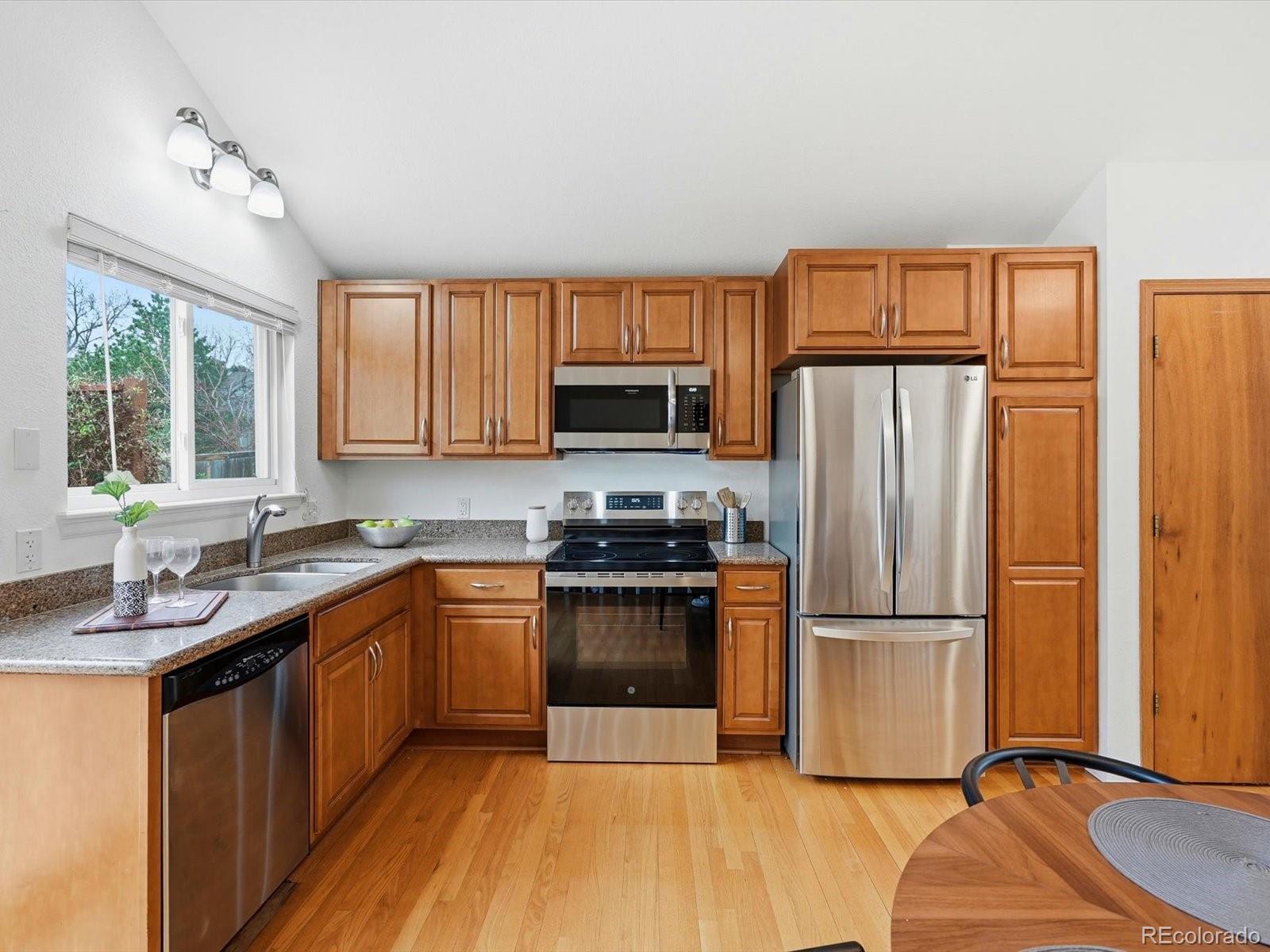 765 Stowe Street Highlands Ranch, CO 80126 - Photo 14 of 43 a kitchen with granite countertop wooden floors stainless steel appliances a sink and a window