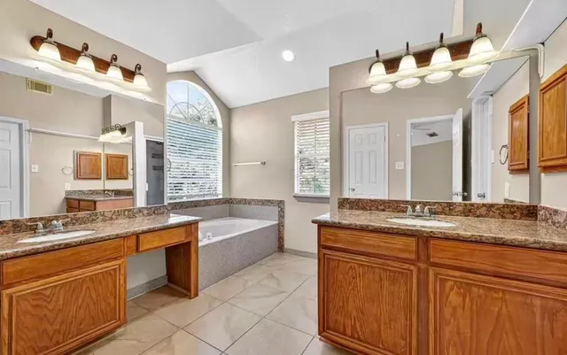 a bathroom with a granite countertop double vanity sink and mirror with bathtub