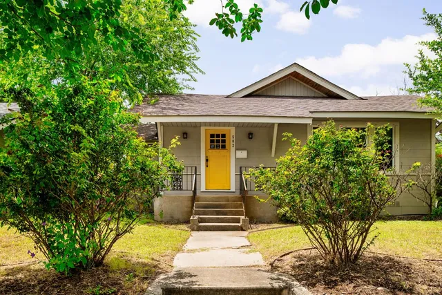 a view of a brick house with potted plants and large trees