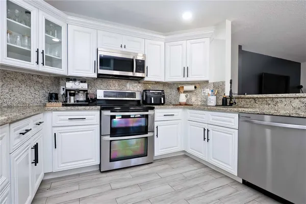 a kitchen with stainless steel appliances granite countertop a stove top oven a sink dishwasher and a microwave oven with white cabinets