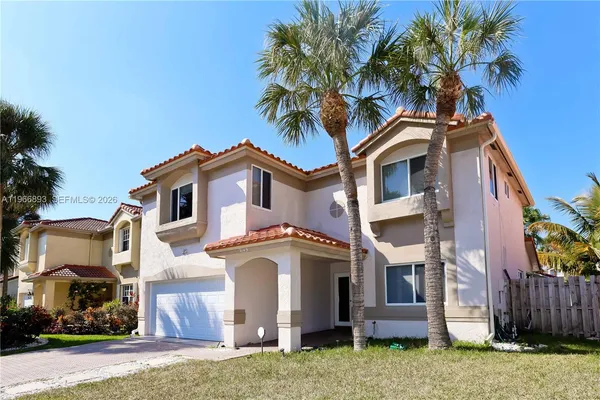 a view of a white house with a small yard and large trees