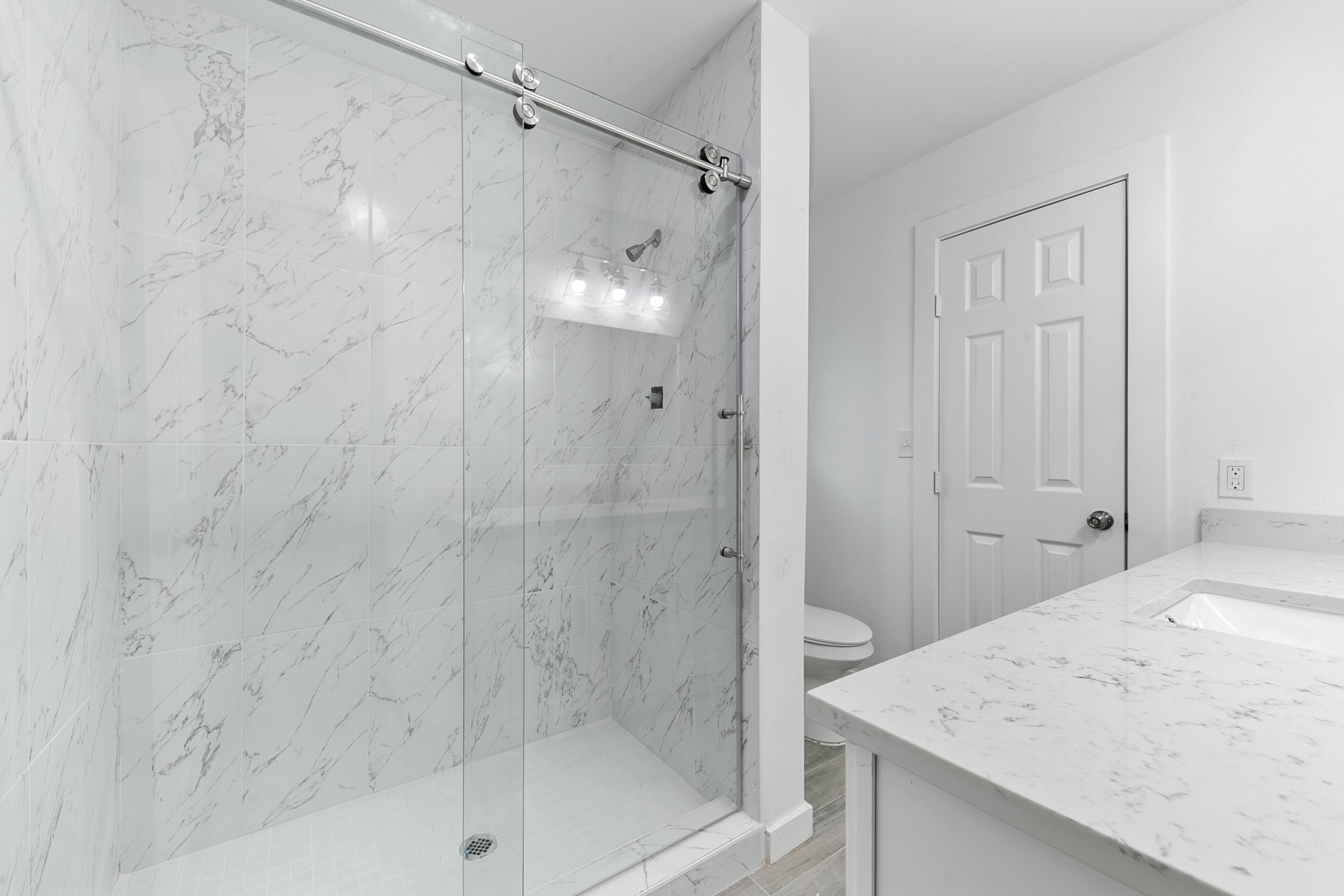 6811 McCullum Road Houston, TX 77489 - Photo 16 of 22 This bathroom features a modern design with a glass-enclosed shower, marble-patterned tiles, and a sleek vanity with a white countertop.
