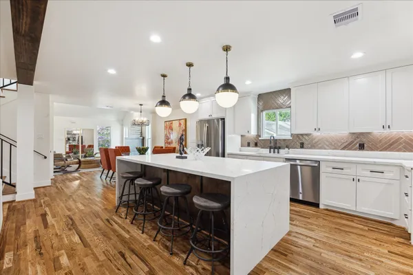 a large kitchen with cabinets a sink a stove and chairs with wooden floor