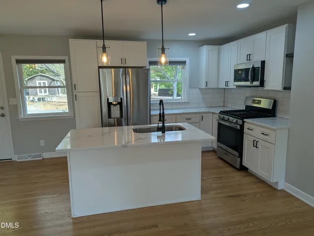 a kitchen with stainless steel appliances granite countertop a sink a stove a refrigerator cabinets and wooden floor