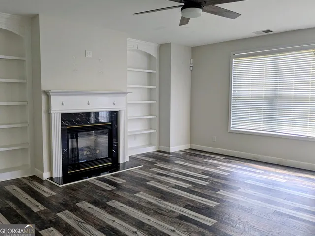 a view of an empty room with wooden floor fireplace and a window