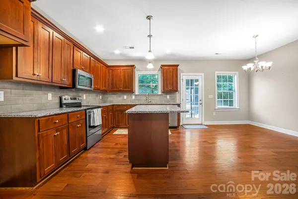 a large kitchen with stainless steel appliances granite countertop wooden cabinets a stove a sink and a large window