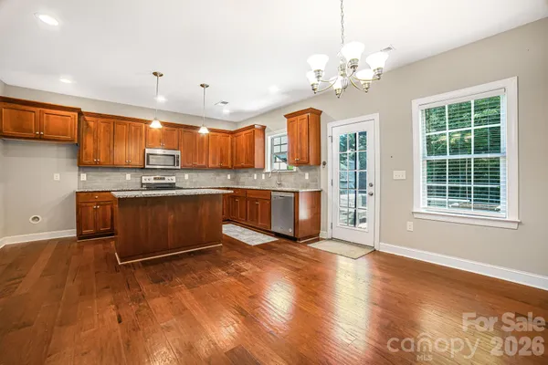 a kitchen with stainless steel appliances granite countertop a stove top oven a sink dishwasher with a dining table and chair with wooden floor