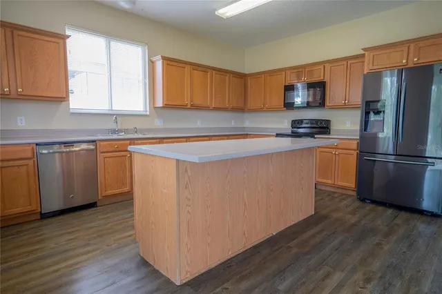 a kitchen with stainless steel appliances granite countertop a refrigerator a sink dishwasher a stove and white countertops with wooden floor