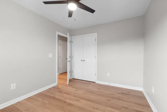 an empty room with wooden floor ceiling fan and window