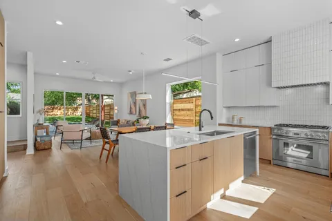 a open kitchen with stainless steel appliances granite countertop a stove top oven a sink dishwasher a dining table and chairs with wooden floor