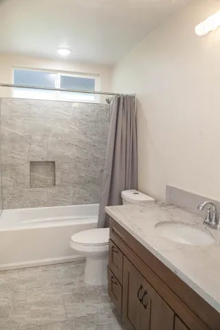 a bathroom with a granite countertop bathtub shower sink vanity and toilet