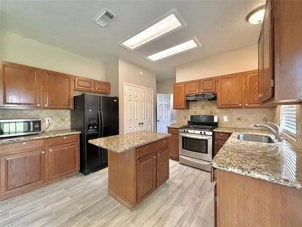 a kitchen with stainless steel appliances granite countertop a stove top oven a refrigerator a sink and dishwasher with wooden floor