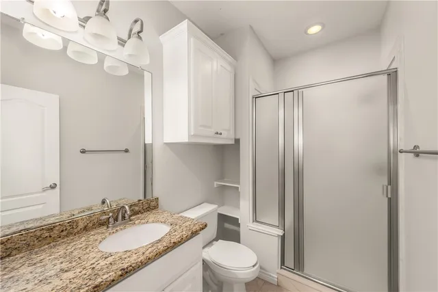 a bathroom with a granite countertop sink a toilet a mirror and shower