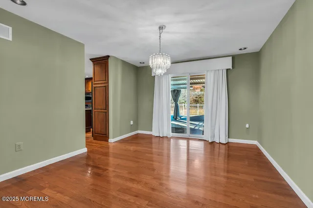 an empty room with wooden floor chandelier and windows