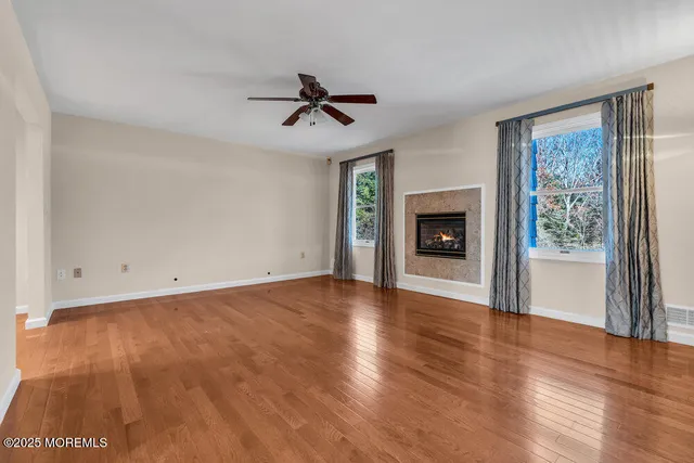 a view of an empty room with wooden floor and a ceiling fan