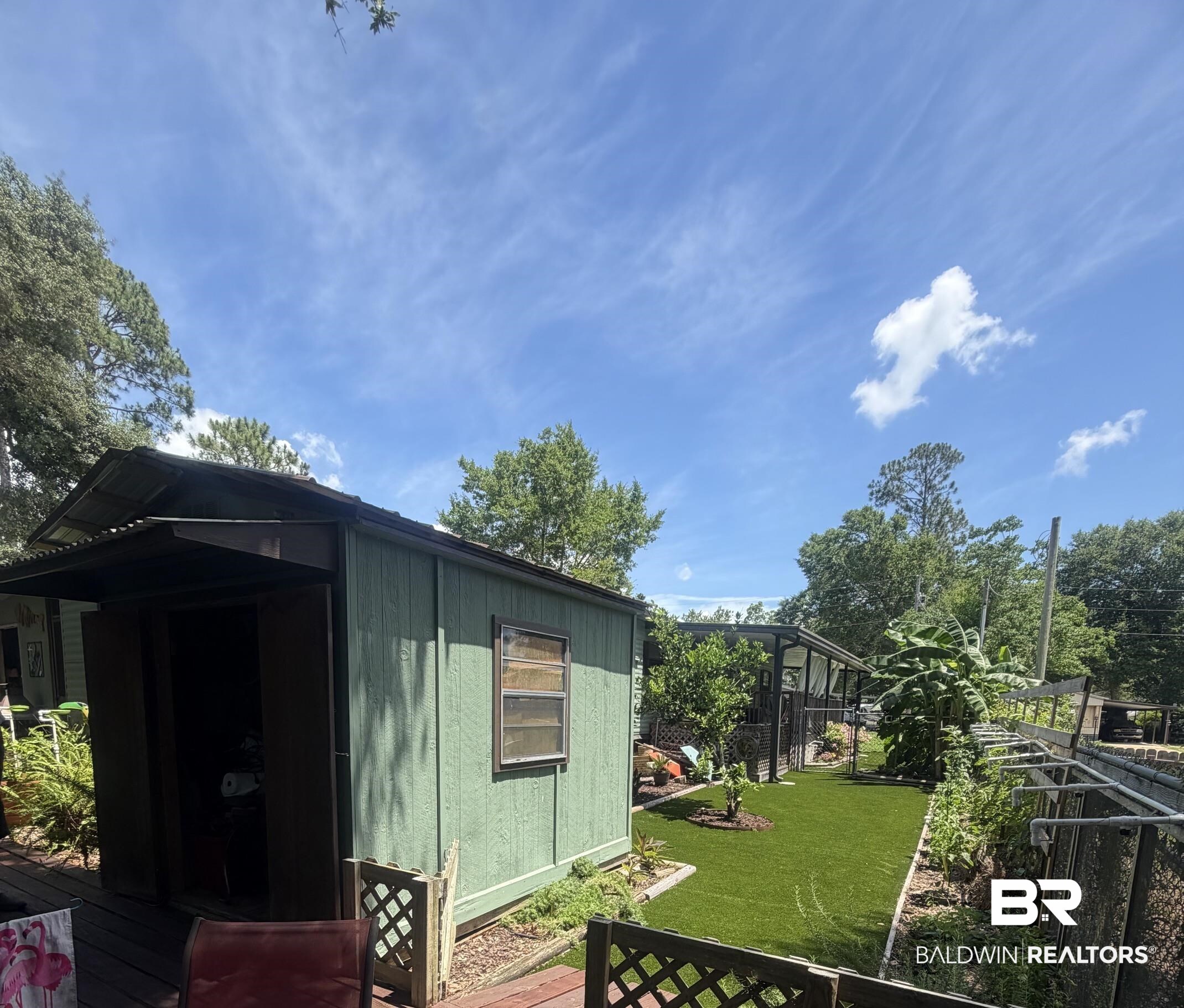 1620 Del Rey Drive Lillian, AL 36549 - Photo 26 of 45 Green-sided outbuilding with a corrugated metal roof and an awning, positioned on a wooden deck